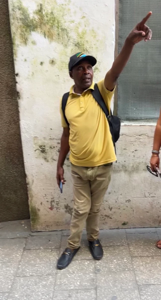 A Tanzanian local guide pointing out a detail along a narrow Stone Town street