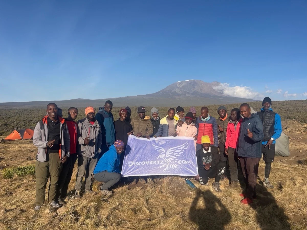 The Tanzanian mountain team gathered at camp beneath Mount Kilimanjaro with a DiscoverTZ banner