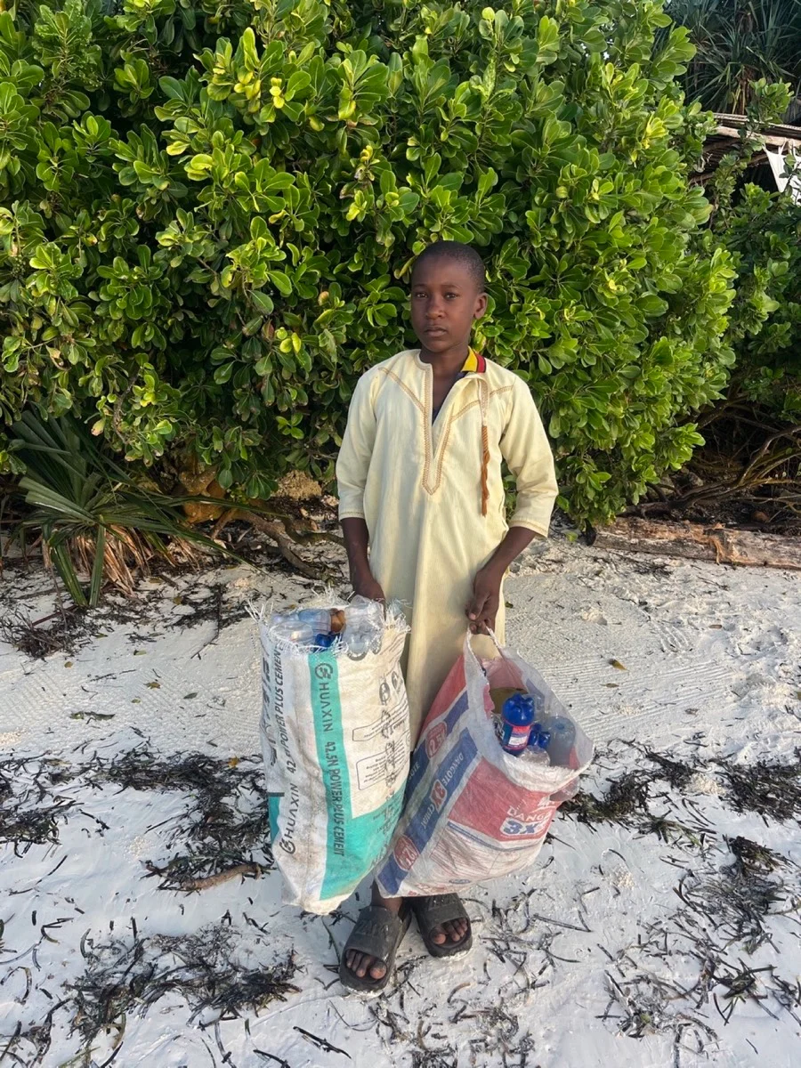 A young Zanzibari boy holding sacks of plastic bottles collected along the beach