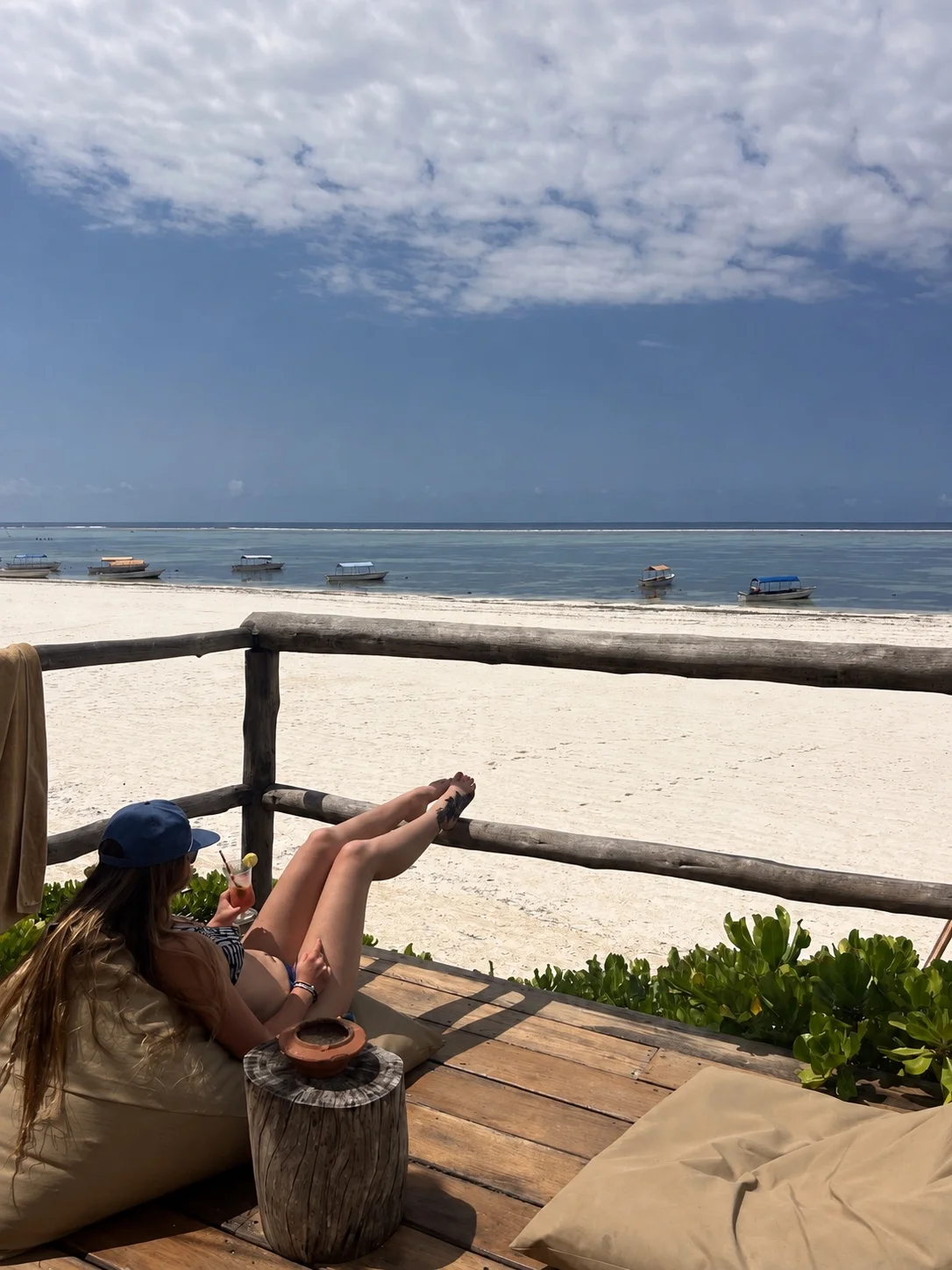 A traveler relaxing with a drink above a white Zanzibar beach and anchored boats