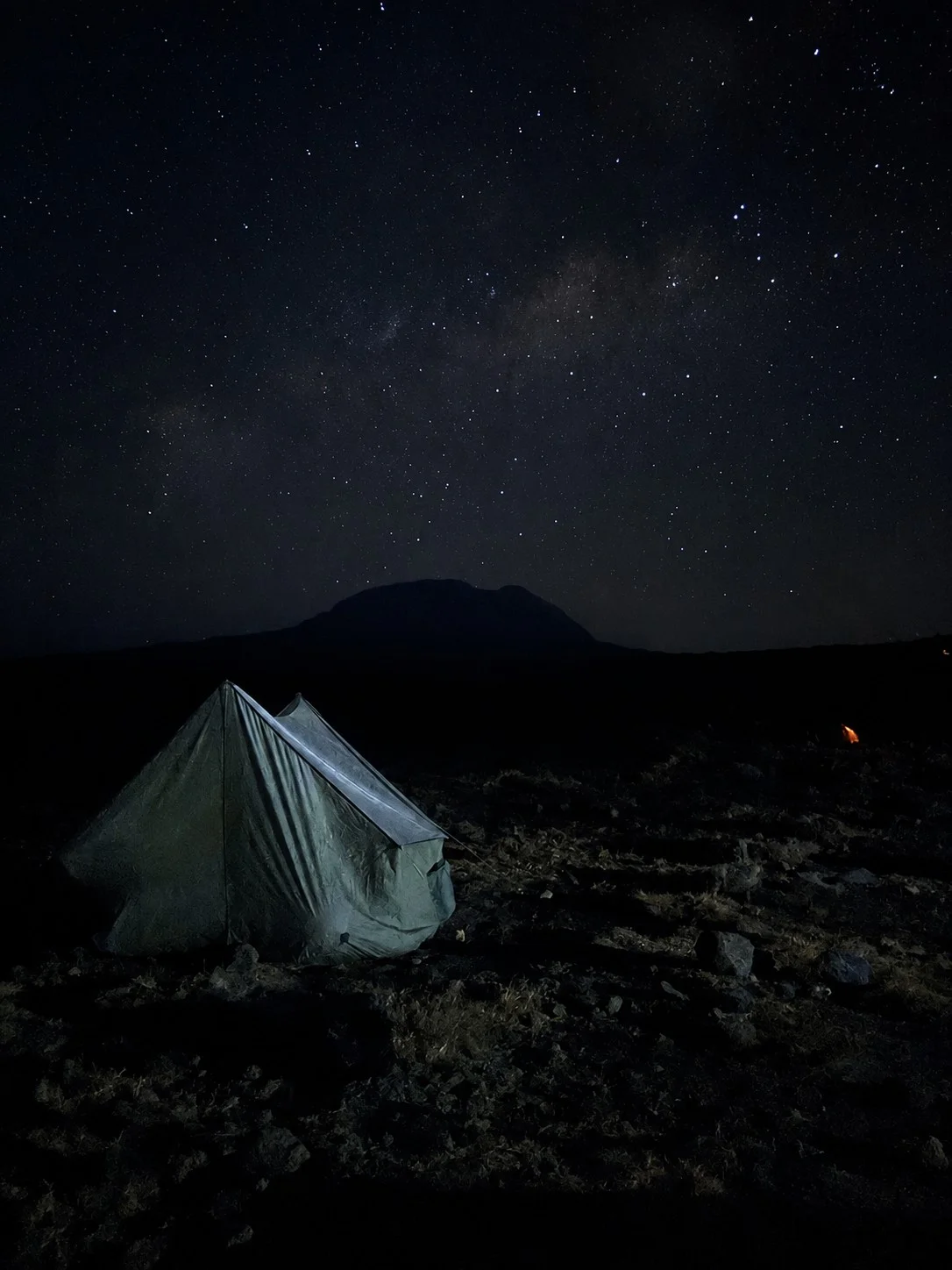 A tent at night beneath a star-filled sky and the silhouette of Mount Kilimanjaro