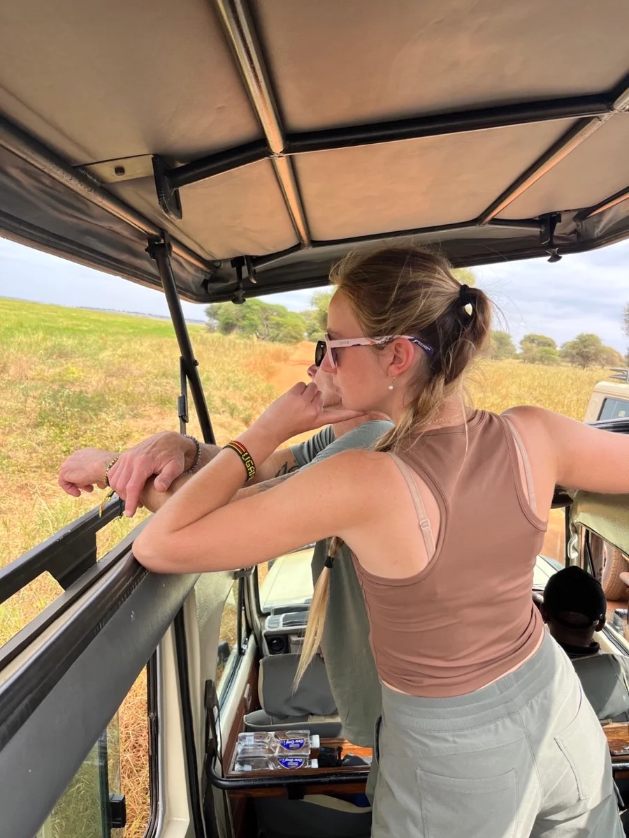 A traveler with a long braid watching the Tanzanian landscape from the open roof of a safari vehicle