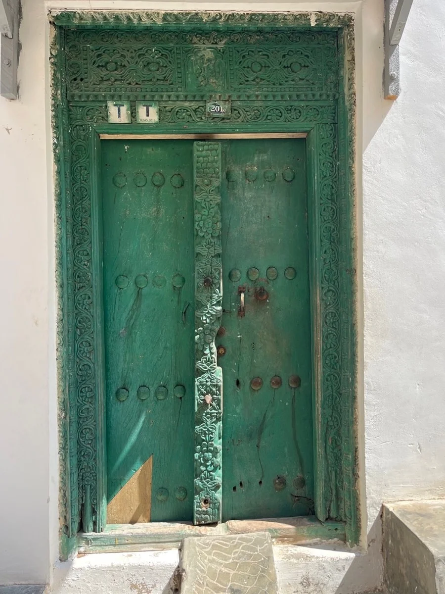 A weathered green carved wooden door in Stone Town