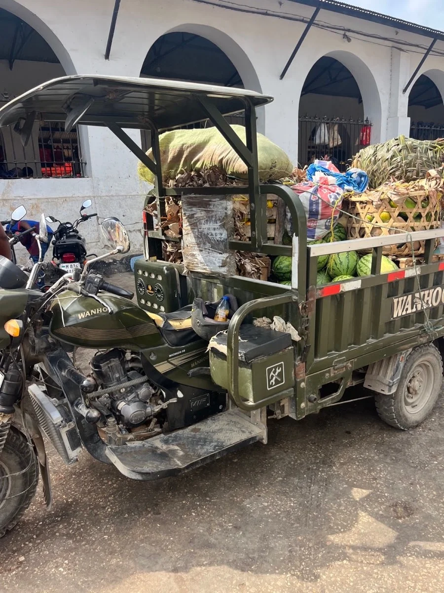A cargo motorcycle loaded with watermelons and woven baskets at a Zanzibar market